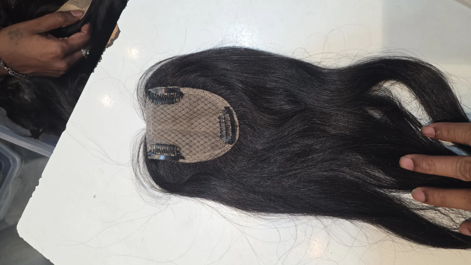Long dark hair topper held open to show its smaller base and clips
